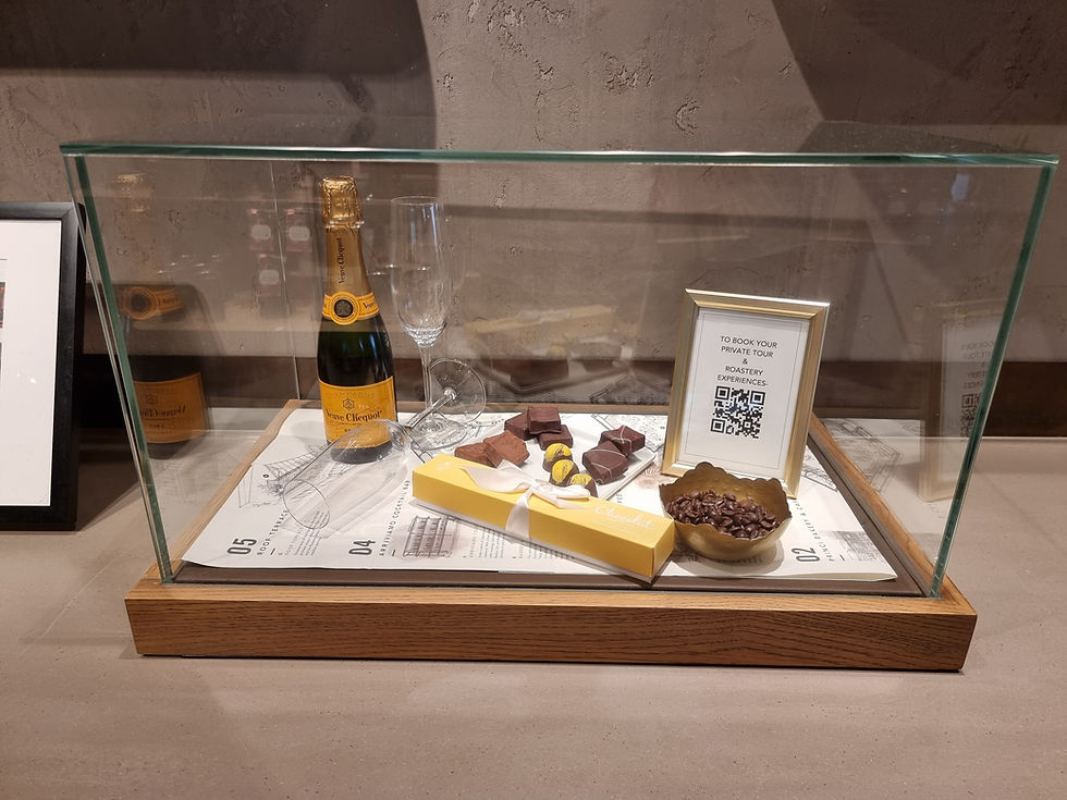 Champagne bottle, chocolates, and glass in display case. Framed sign with QR code and "To book your private tour". Elegant, inviting setting.