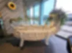 A sculpture of a creature made from white plates, teacups on its back, with leafy decor, in a modern room with large windows and herringbone tiles. World of Wedgwood shop interior.