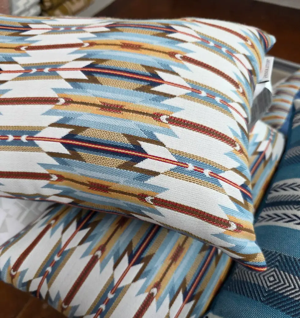 Stacked pillows with colorful geometric patterns in blue, brown, and white, set on a wooden surface, creating a cozy atmosphere at Pendleton Woolen Mill Tour Washougal store.