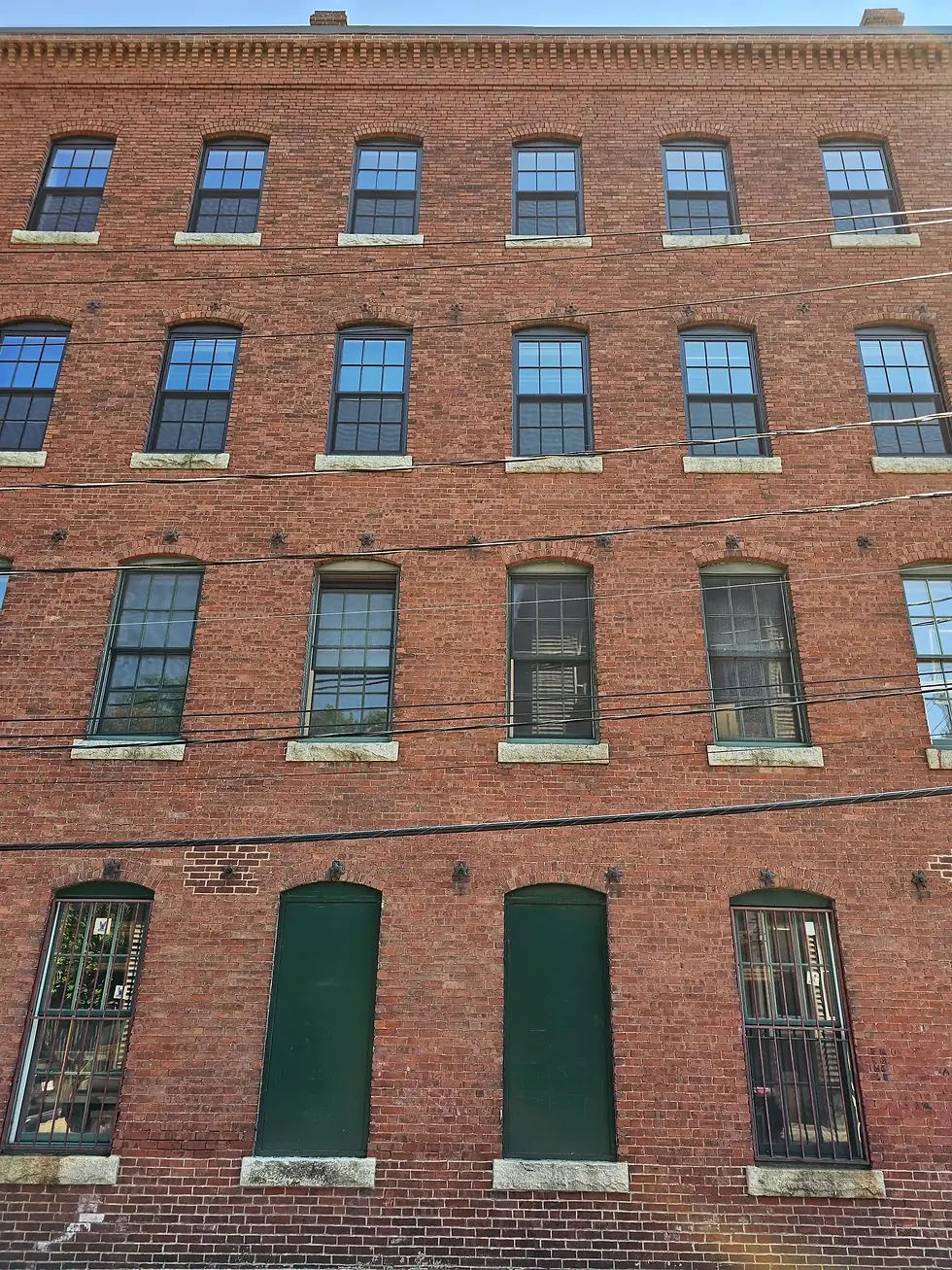 Red brick building with three floors of large windows, some barred. Clear blue sky above. Urban, historic feel. No visible text.