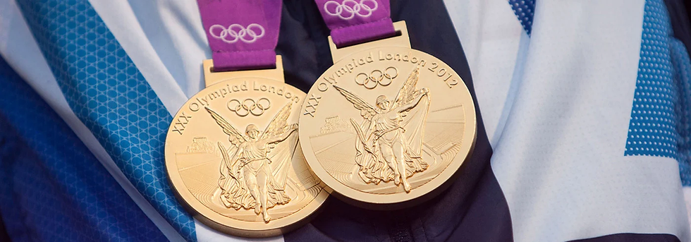 Two gold medals from the 2012 London Olympics on a blue and white fabric background. The medals feature an angel and the Olympic rings.