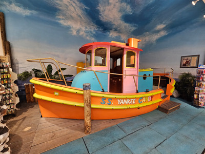 a children's climbing frame in the shape of a boat sits in the shop. the boat has an orange hull and is called the ss yankee