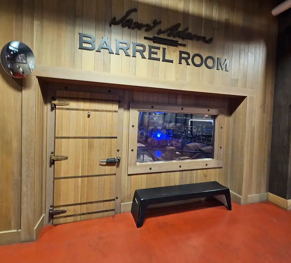 Wooden "Barrel Room" door with metal hinges, window displaying blue-lit equipment inside, and a black bench on a red floor. Samuel Adams Boston Brewery Tour