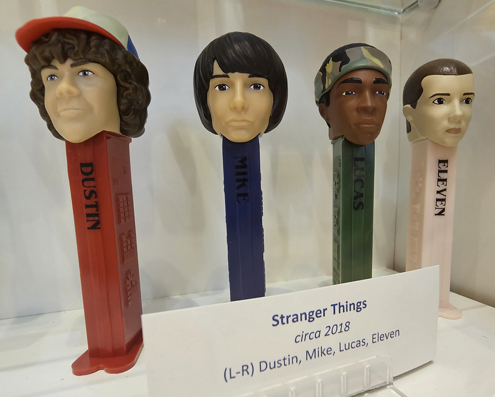 Four Pez dispensers with character heads from Stranger Things: Dustin, Mike, Lucas, and Eleven. Labels and display tag included.