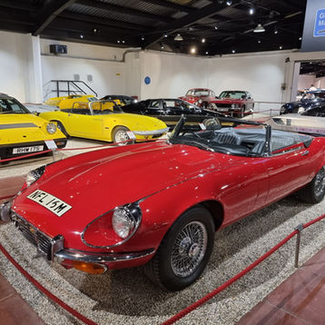 Classic cars displayed in Haynes Motor museum setting, featuring a red convertible and yellow cars. "Great British Marques" sign above; "Exit" sign in back. all this is at the Haynes Motor Museum visitor centre