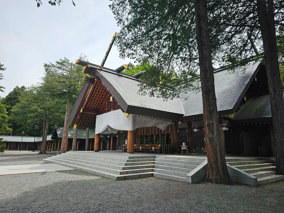 Japanese Hokkaido Jingu shrine with a sloped roof amid tall trees, set on stone steps, creating a serene and traditional atmosphere in the greenery.
