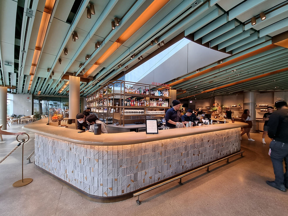 Modern cafe with a stylish bar counter. Staff in black uniforms work behind the bar. Geometric ceiling design and warm lighting set the mood.
