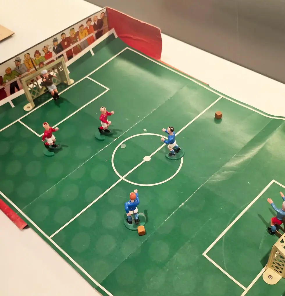 Miniature tabletop soccer game on a green pitch, with red and blue players near the goals and small crowd cutouts in the stands at the FIFA Museum.