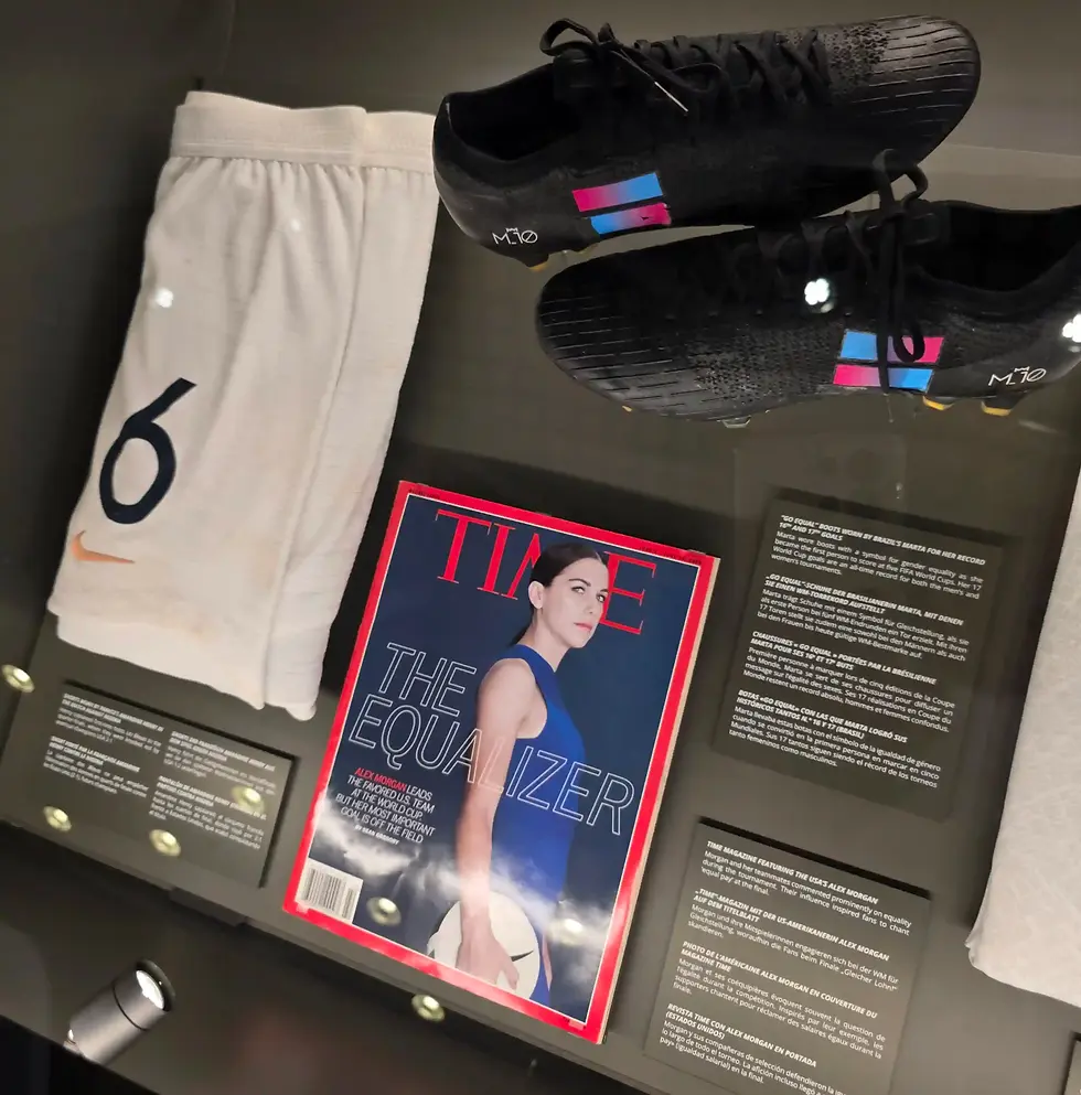Display case with white soccer shorts, black cleats, and a TIME cover of Alex Morgan titled The Equalizer at the FIFA Museum.