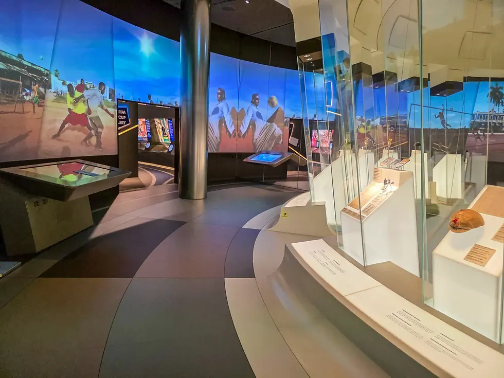 Modern FIFA museum exhibit with FIFA Cup history, soccer photos, glass cases, and display screens in a sleek blue-lit gallery.