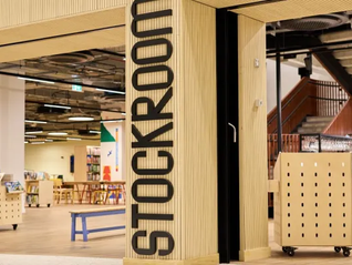 Entrance to a modern library with a sign reading "Stockroom." Bright interior, wooden decor, colorful chairs, and bookshelves visible.