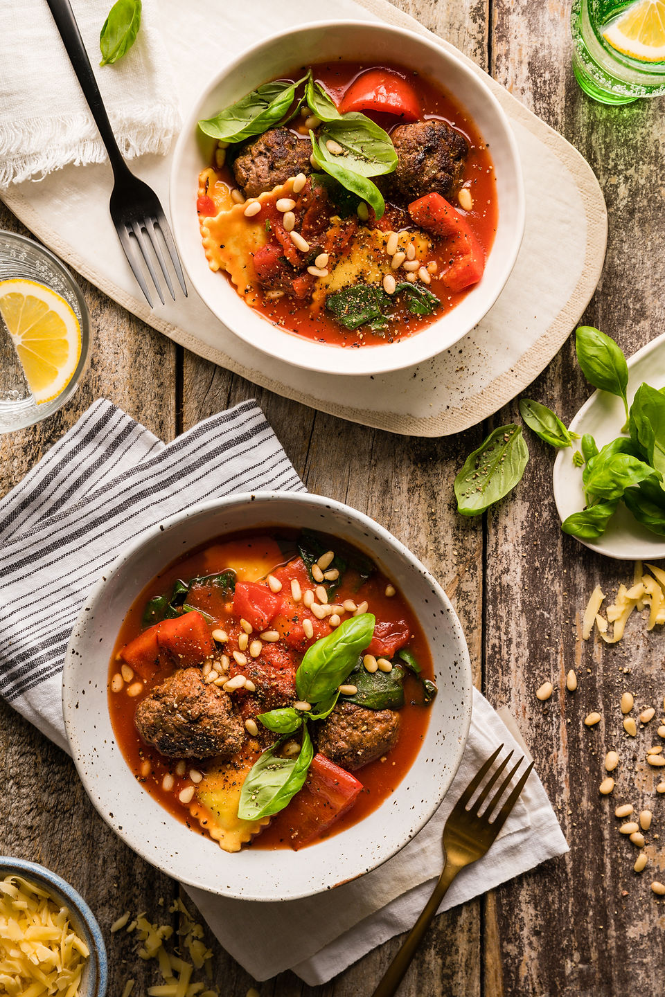 Two bowls of meatball and ravioli with pine nuts and basil.