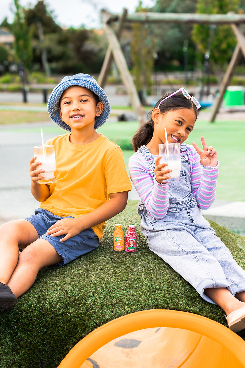 Two kids in a playground drinking from a glass.