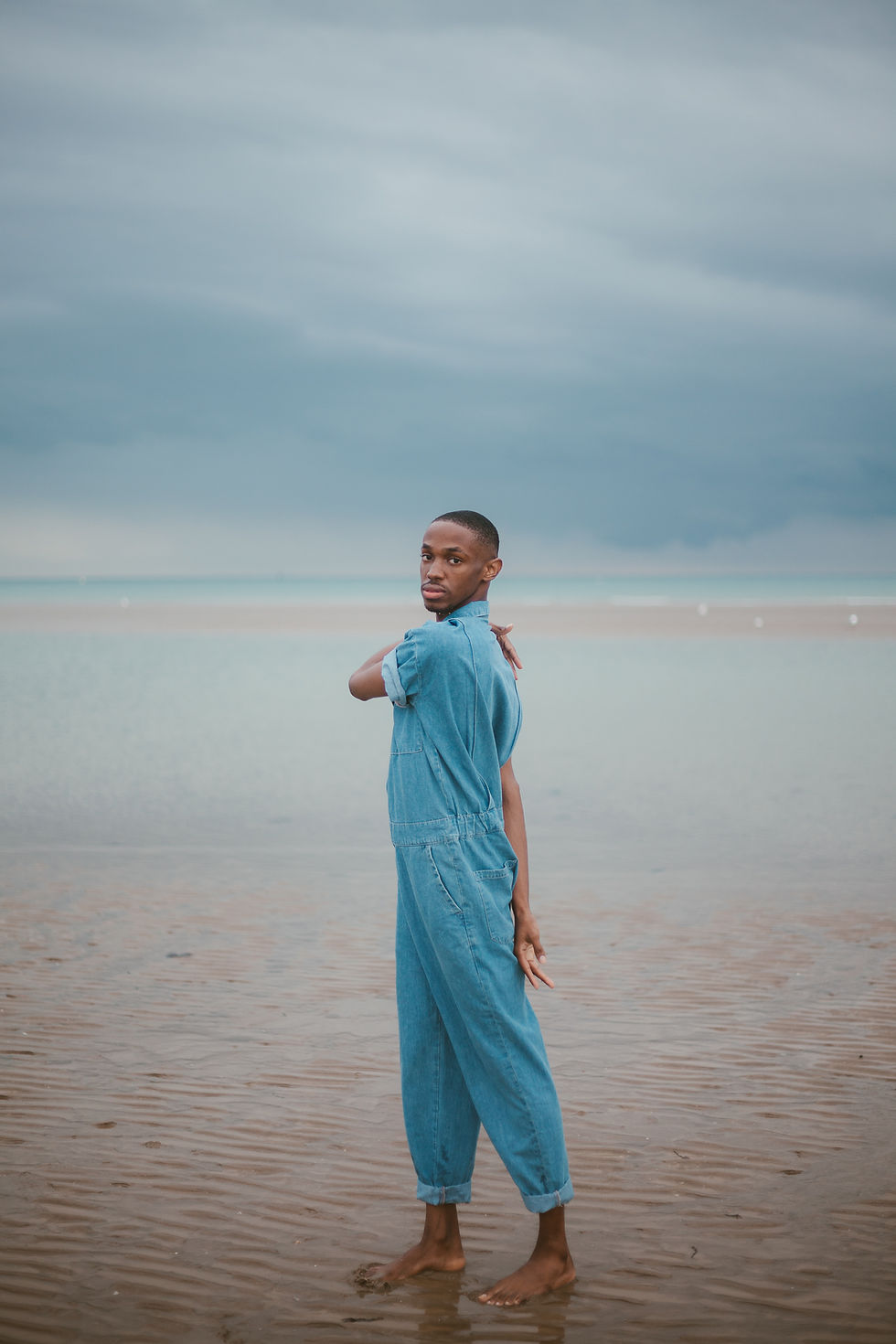 A young man is standing on the seashore in a denim jumpsuit