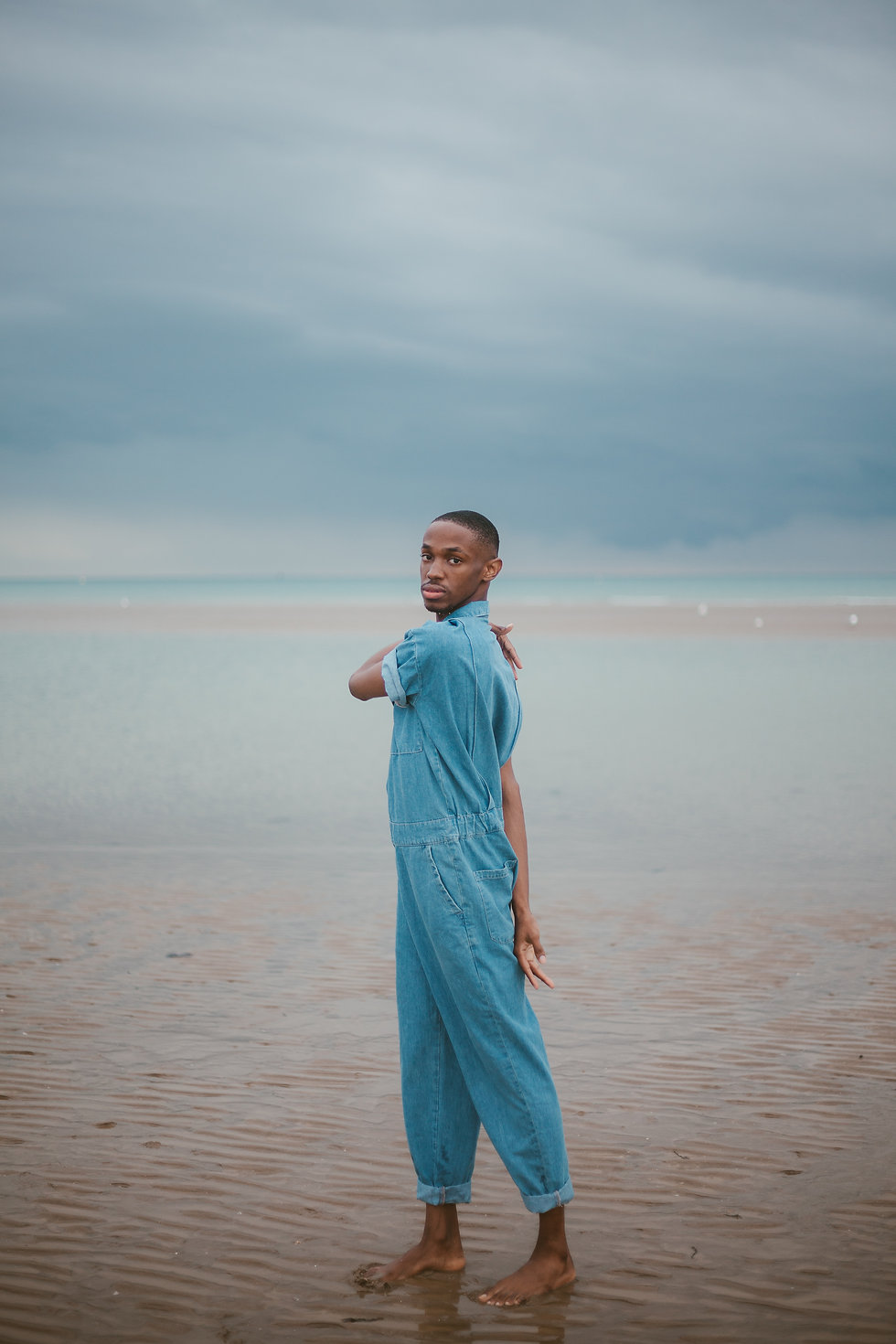 A young man is standing on the seashore in a denim jumpsuit
