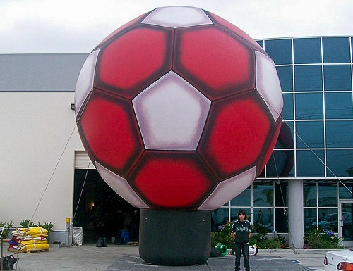 Large red inflatable soccer ball landmark installed outside a venue building for a soccer event.