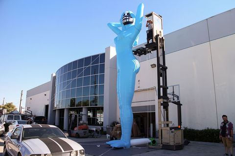 Tall blue inflatable humanoid figure with a futuristic design, installed outdoors at an event setup.