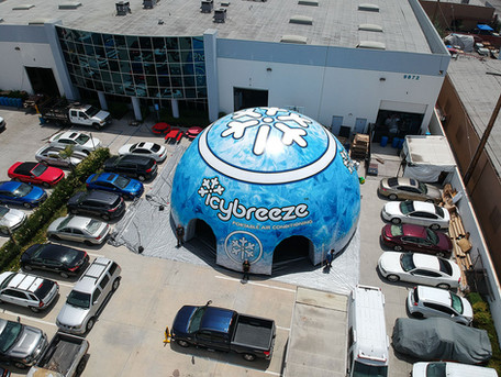 Branded inflatable dome commercial tent set up outdoors in a parking lot with full-surface graphics and a marked entrance.