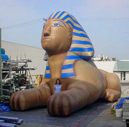Giant inflatable sphinx shown from a side angle on a tarp in an outdoor staging area.