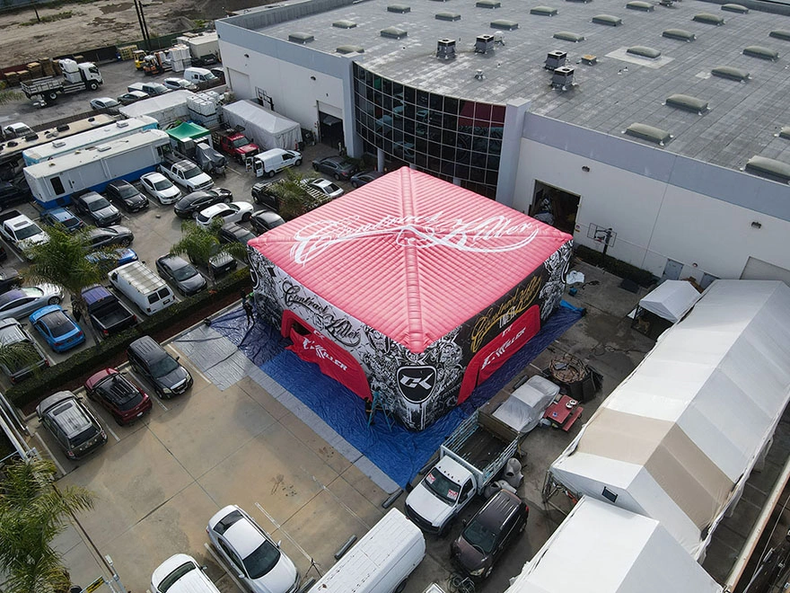 Wide aerial view of a 45x45 inflatable commercial tent with roof branding installed in a parking lot footprint near a large building.