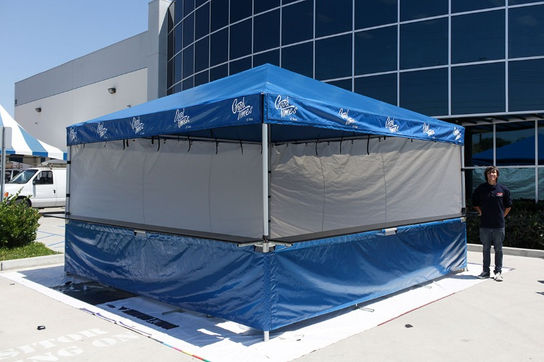 Blue commercial tent with full printed branding and sidewall enclosure set up outside a modern building