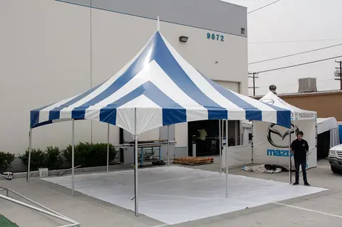 Blue and white high peak frame tent set up outside a commercial building.