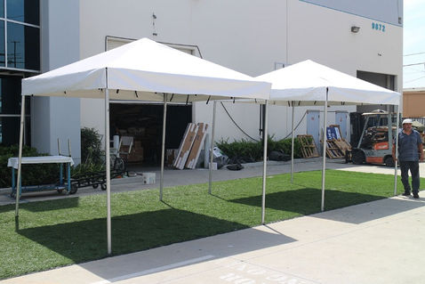 Two white 10x10 pop up tents set up outside a warehouse.