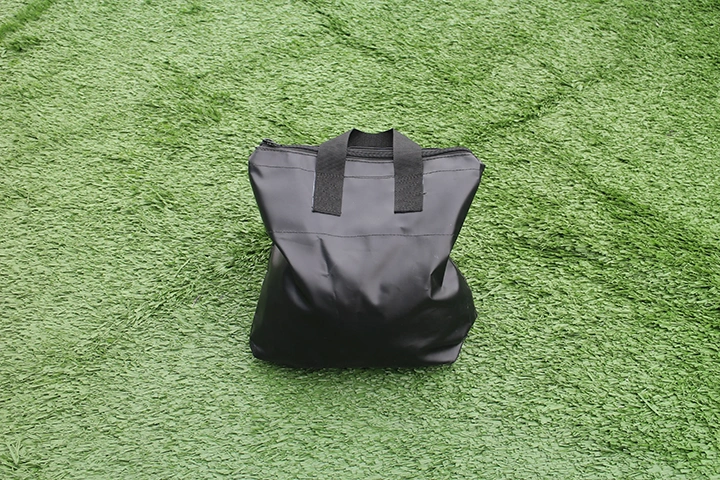 Black sandbag with reinforced handles shown at an angle on artificial grass