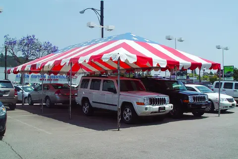 Red and white striped frame tent rental covering parked vehicles at an outdoor lot.