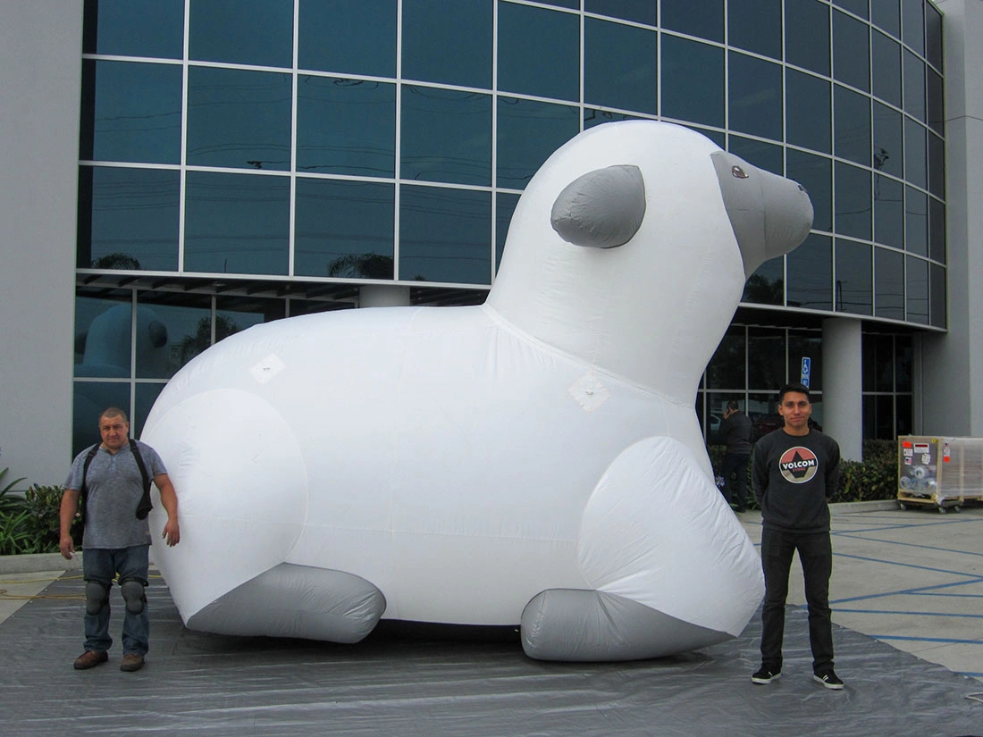 White giant inflatable lamb rental display with gray face and ears set outdoors with two people standing beside it for scale