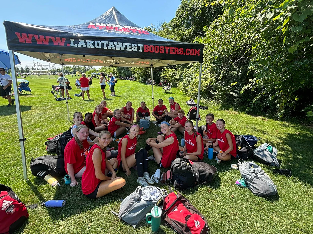 Lacrosse team seated under a custom printed canopy at a sports field.