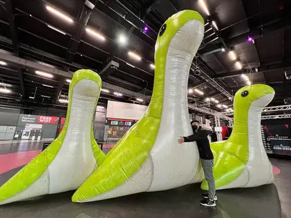 A giant green and white custom inflatable dinosaur displayed indoors, with a person posing next to it for scale.