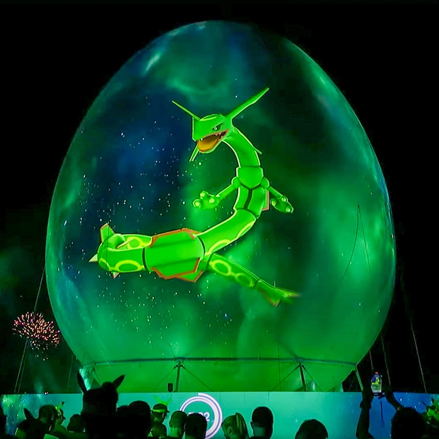 Close up of a projection mapped inflatable sphere showing vivid green visuals at night with audience silhouettes at the bottom.