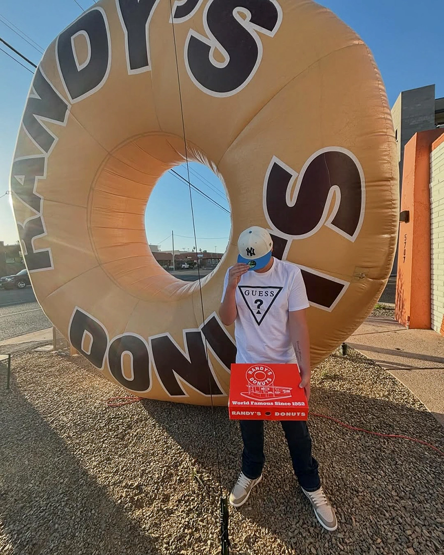 Person standing in front of a giant inflatable donut replica inspired by iconic roadside donut architecture