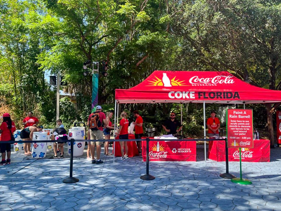 A 10x10 red pop-up canopy with Coca-Cola Florida branding at an outdoor promotional event. Staff members interact with attendees, while branded sidewalls and signage enhance the booth’s visibility.