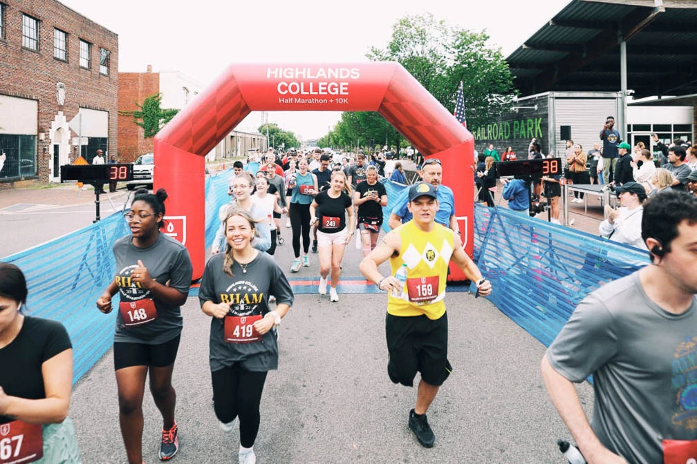 Runners crossing under a red inflatable finish line arch with blue chute fencing at a 5K race