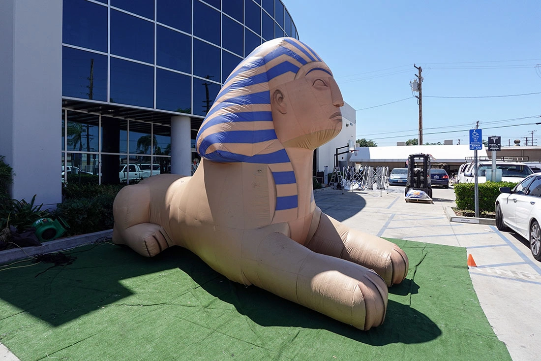 Large inflatable sphinx event prop resting on a green tarp near a warehouse driveway during setup.