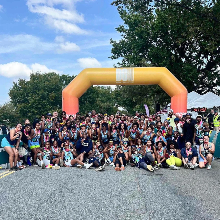 Group photo at a 5K event in front of an orange inflatable race arch near the finish line