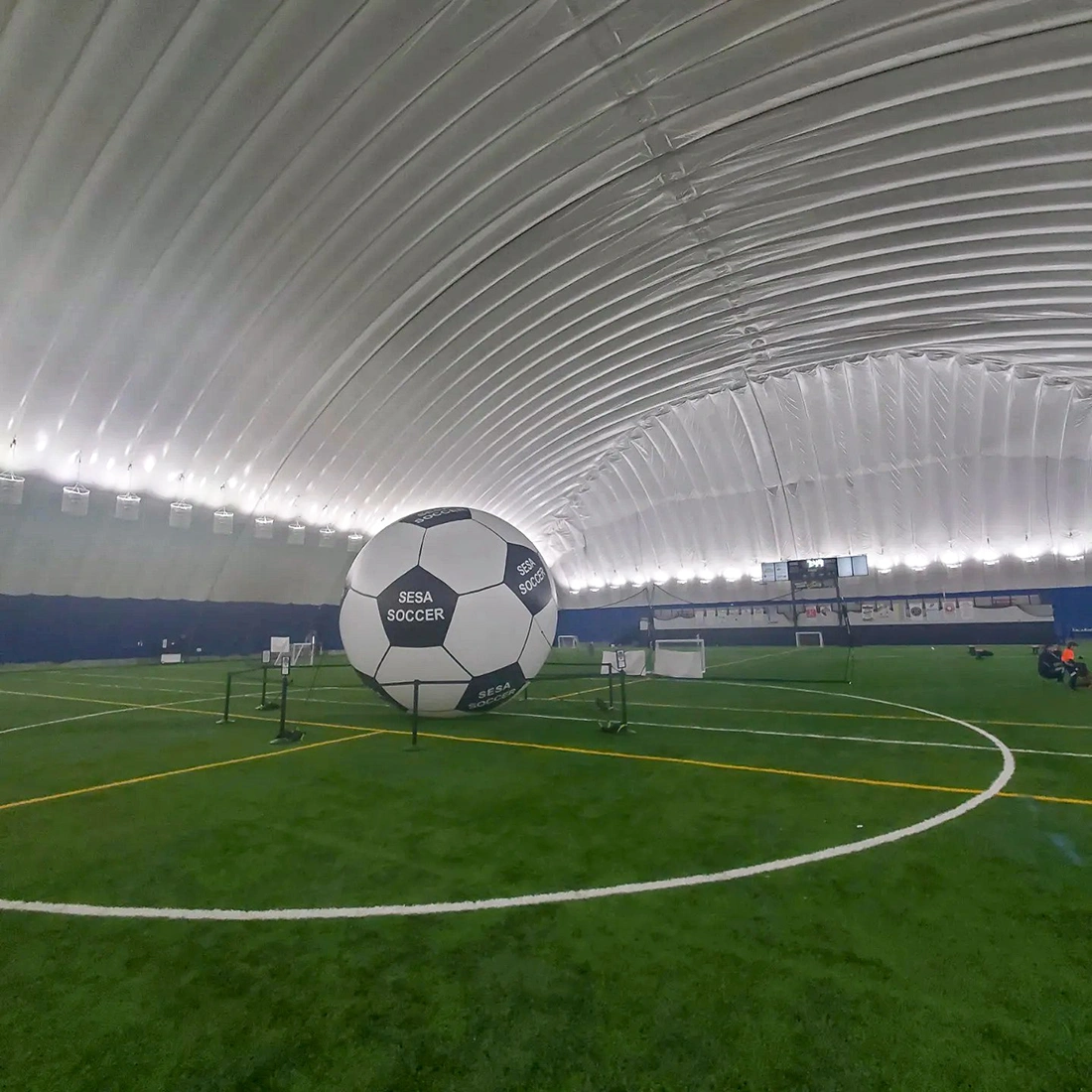An oversized inflatable soccer ball displayed inside an indoor sports dome, serving as a centerpiece for a soccer-themed event environment.