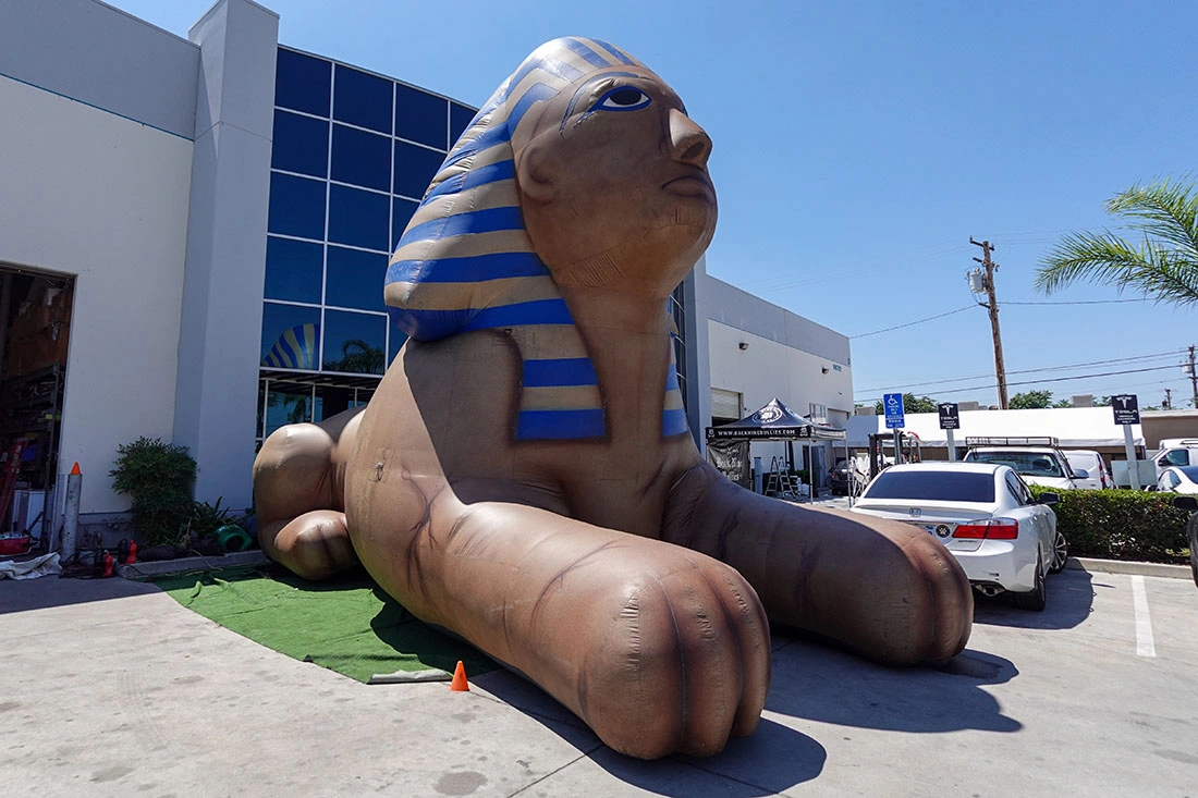 Giant inflatable sphinx in a parking lot outside a commercial building, positioned as a themed landmark display.