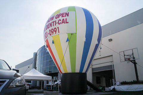 Large inflatable hot air balloon with multicolor stripes and promotional text, set up outside a commercial building.