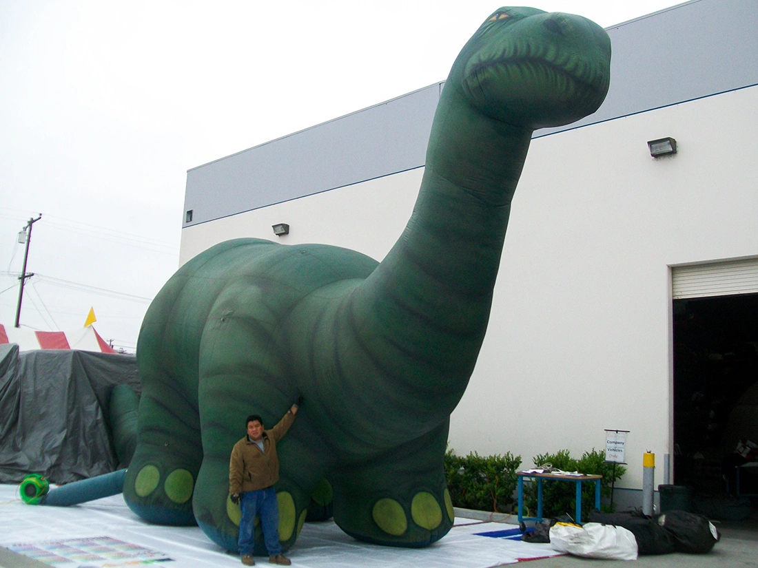 Custom giant inflatable brontosaurus dinosaur outside a warehouse during setup, showing large-scale inflatable dinosaur footprint and height