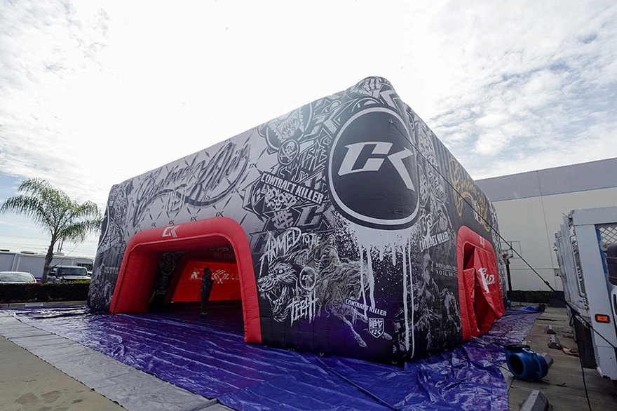 Angled view of a 45x45 inflatable commercial event tent with full-wrap graphics and red arched entrances, staged outdoors on tarps.