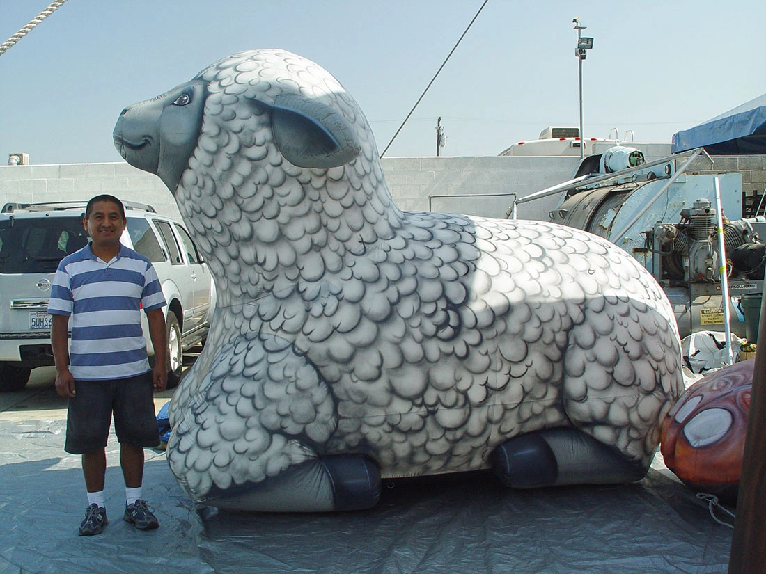 Giant inflatable lamb rental display with gray wool texture print on a tarp with a person standing beside it for scale