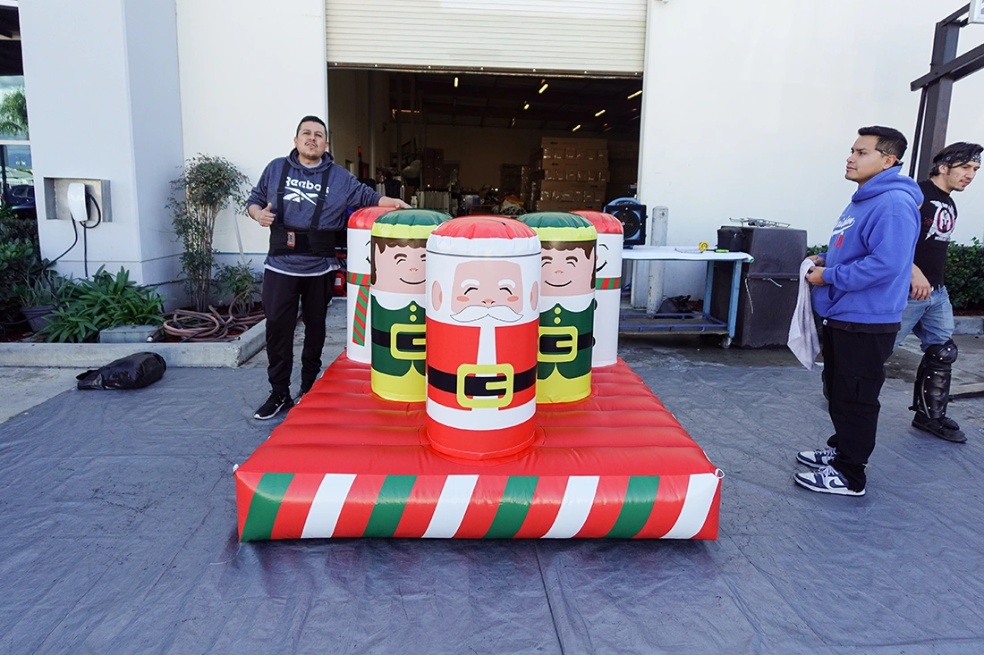 Christmas inflatable ring toss game with Santa and elf targets on a striped inflatable base set up outdoors with staff nearby.