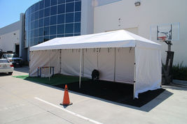 White commercial canopy tent with side and back walls and open front, placed on turf with a cone
