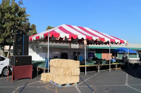 Red and white striped event tent rental set up with hay bales and a speaker system for an outdoor festival.