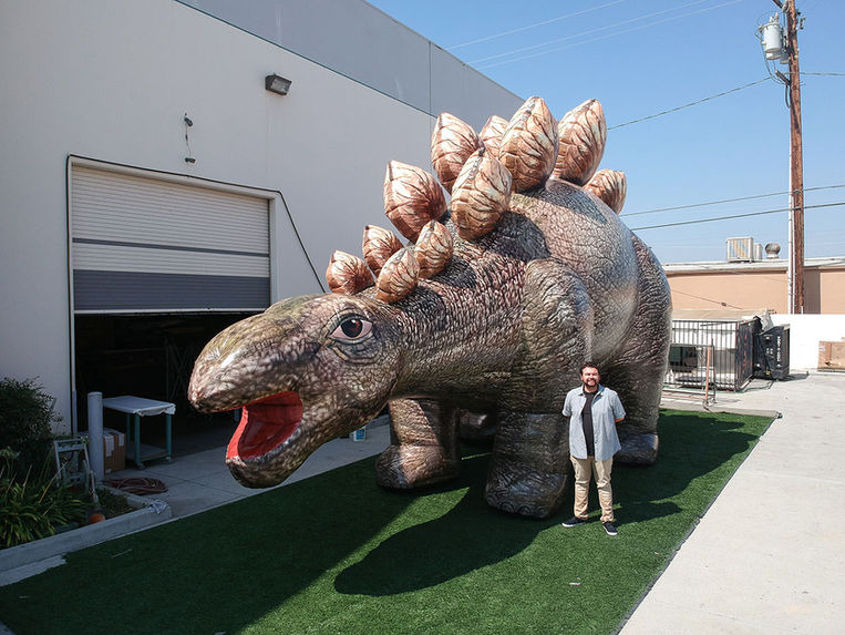 Museum-quality inflatable dinosaur display with realistic artwork shown beside a person to demonstrate the scale of a large dinosaur exhibit.