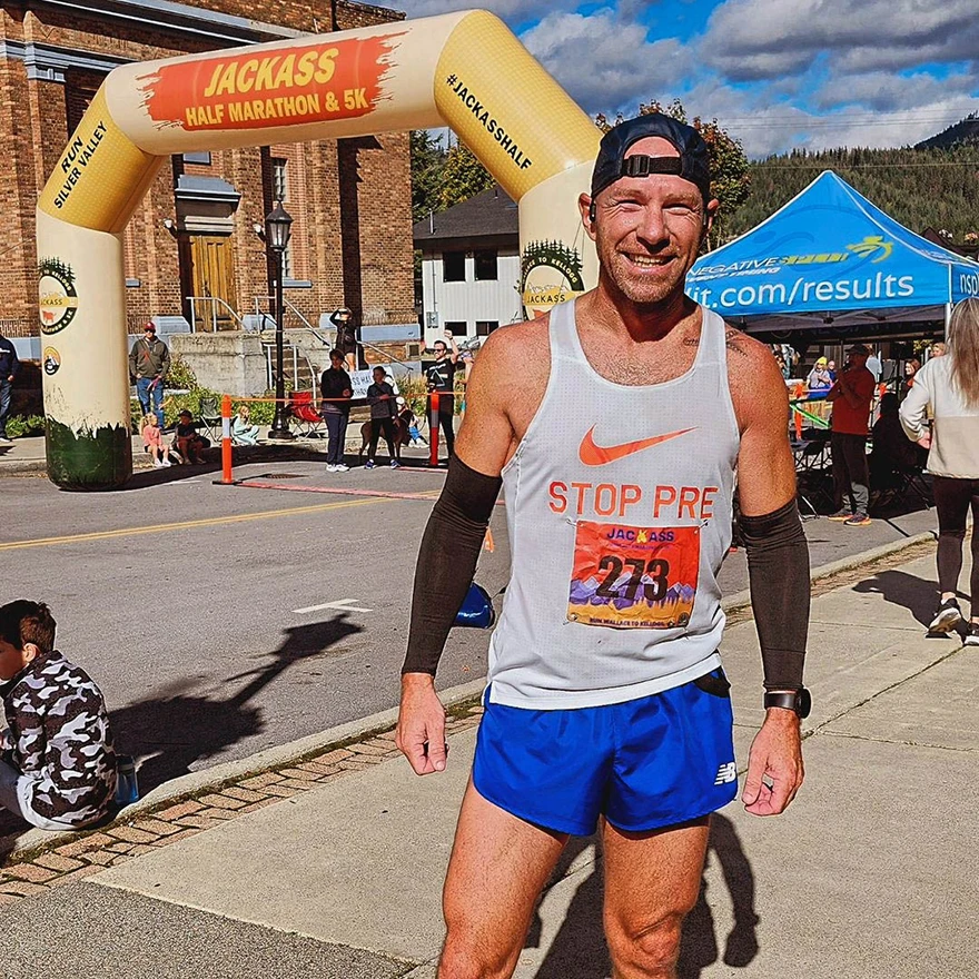 Runner posing in front of a tan inflatable 5K race arch at a road race event