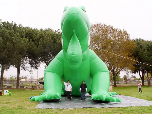 Front view of a giant inflatable iguana set up in a park with people standing in front for scale.